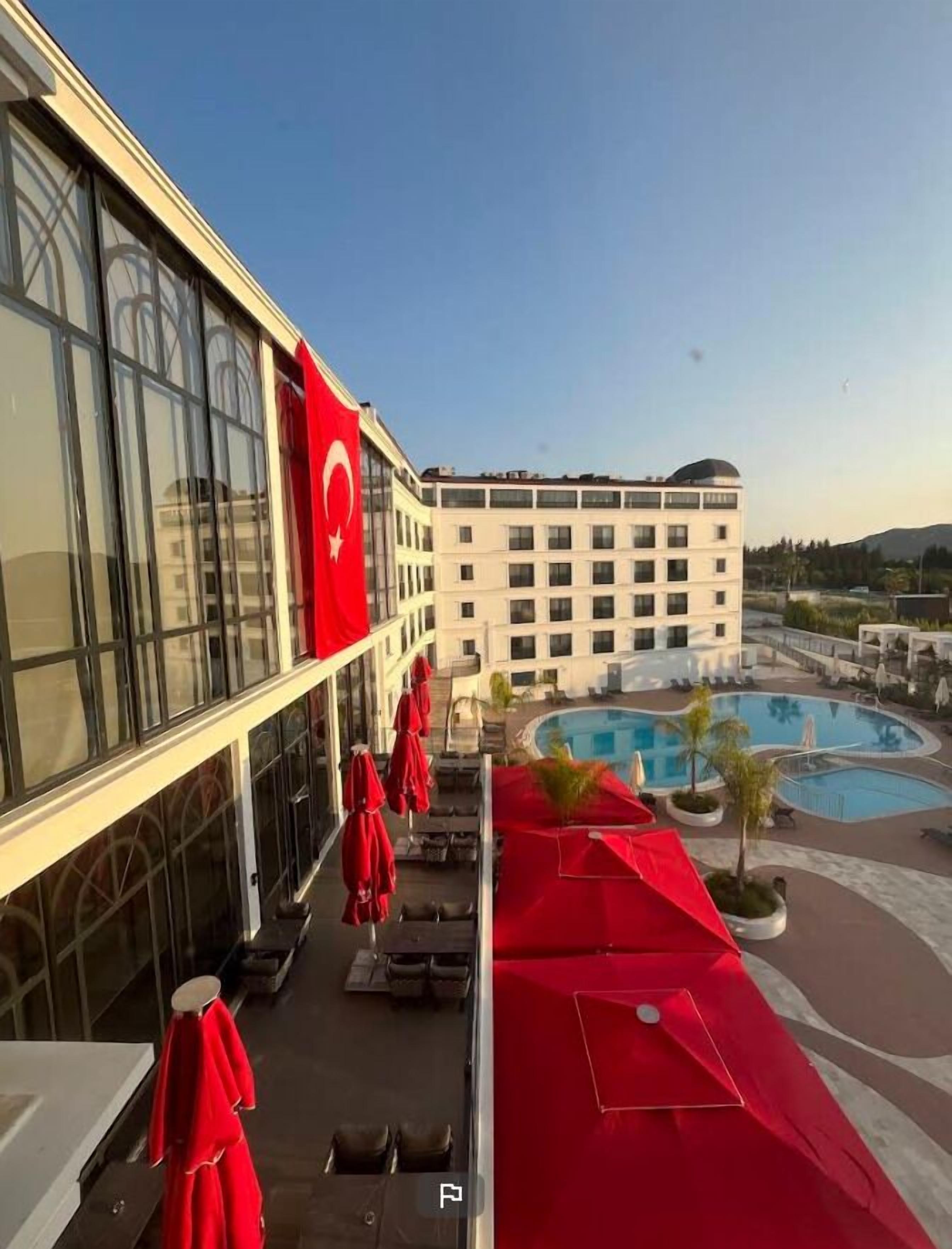 Un hotel con zona de piscina, sombrillas rojas y una bandera.