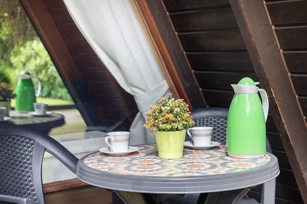 A round table with a patterned tablecloth, a green coffee pot, a white cup, and a potted plant. - Holiday Home 'Ferienhäuser Am Waldschlößchen' with Mountain View, Private Terrace & Garden (Langelsheim)