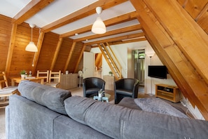 Une pièce de style « loft » avec un canapé, des fauteuils, un téléviseur et des poutres en bois.