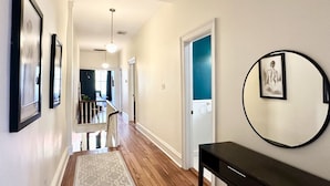 A hallway with a patterned rug, a round mirror on the wall, and a staircase leading to another room.