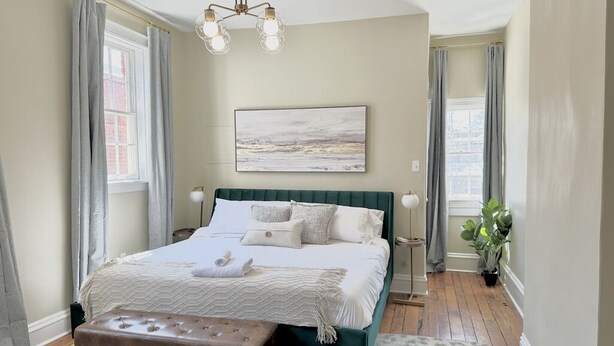 A bedroom with a large bed, a bench, a painting, and a potted plant.