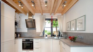 Een moderne keuken met witte kasten, roestvrijstalen apparatuur, een houten plafond en een raam met gordijnen.