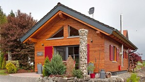 Een houten lodge met een stenen pilaar, een stenen muur en een grindpad.