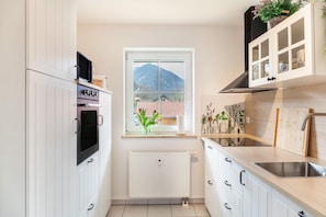 A kitchen with white cabinets, a window with a mountain view, a radiator, and a sink. - Holiday Apartment "Fuchsbau" with Mountain View, Balcony & Wi-Fi (Oberau)