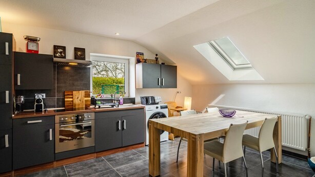A modern kitchen with dark cabinetry, a wooden dining table, and a skylight. - Holiday Home 'Krummes Häusschen An Der Nordsee' with Terrace and Garden (Großheide)