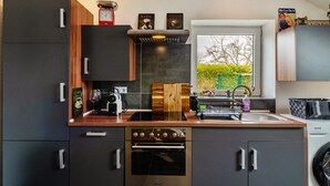 A modern kitchen with a built-in oven, a coffee machine, and a window with a view of greenery. - Holiday Home 'Krummes Häusschen An Der Nordsee' with Terrace and Garden (Großheide)