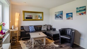 A modern living room with a sofa, a coffee table, a chair, and artwork on the walls. - Holiday Home 'Krummes Häusschen An Der Nordsee' with Terrace and Garden (Großheide)