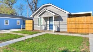 Une maison de plain-pied avec un toit gris, une porte bleue et une véranda blanche.