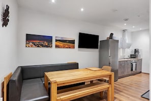 A modern living room with a sofa, wooden table, and kitchen area with appliances.