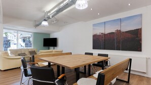 Une salle de réunion moderne avec une table en bois, des chaises noires, un banc, un grand tableau et un téléviseur fixé au mur.