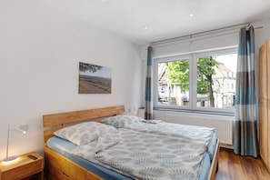 A bedroom with a wooden bed, a nightstand with a lamp, a window with curtains, and a city view.