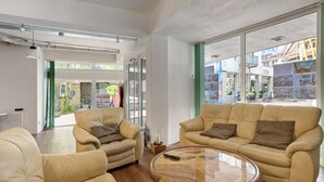 Un vaste espace de vie comprenant deux canapés beige, une table basse en bois et de grandes fenêtres donnant sur la rue.
