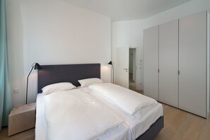 Un dormitorio moderno con una cama, lámparas de noche, una mesita de madera y un armario.