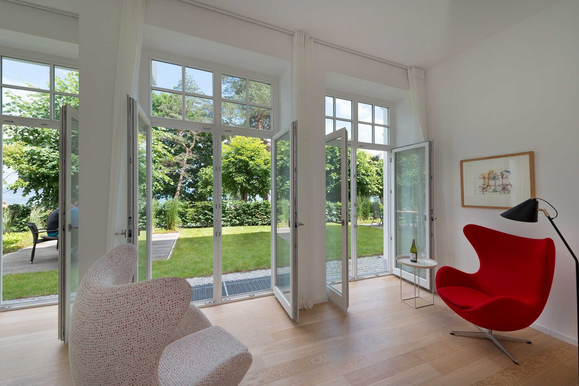 Een ruime kamer met grote schuifdeuren naar een tuin, een rode stoel en een ingelijst kunstwerk aan de muur.