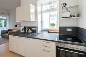 Une cuisine moderne avec des meubles blancs, un plan de travail noir, une cuisinière intégrée et une fenêtre donnant sur un paysage verdoyant.