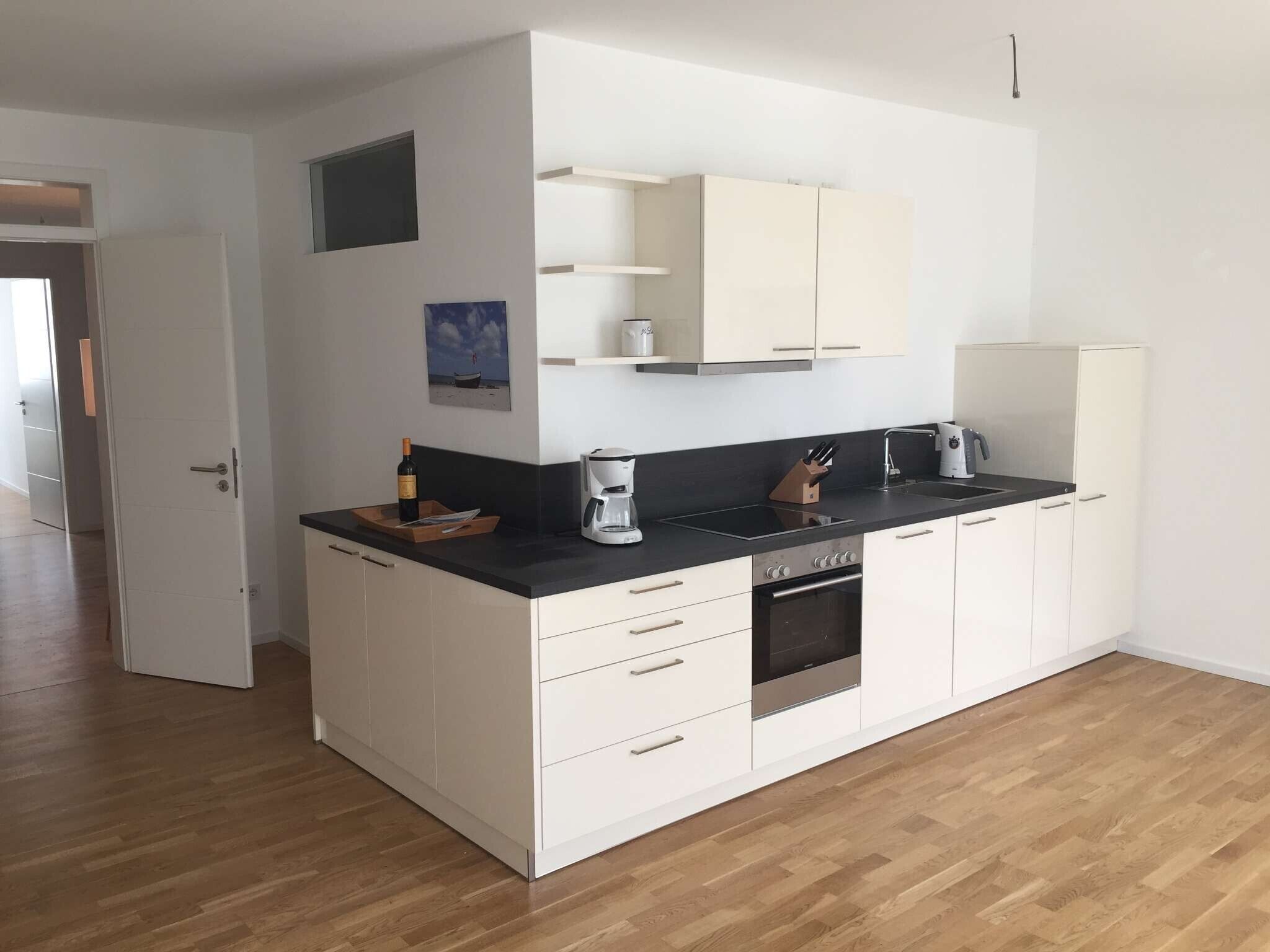 A modern kitchen with white cabinets, a black countertop, a coffee maker, and a wine bottle.