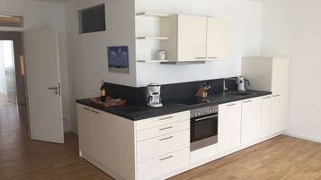 A modern kitchen with white cabinets, a black countertop, a coffee maker, and a wine bottle.
