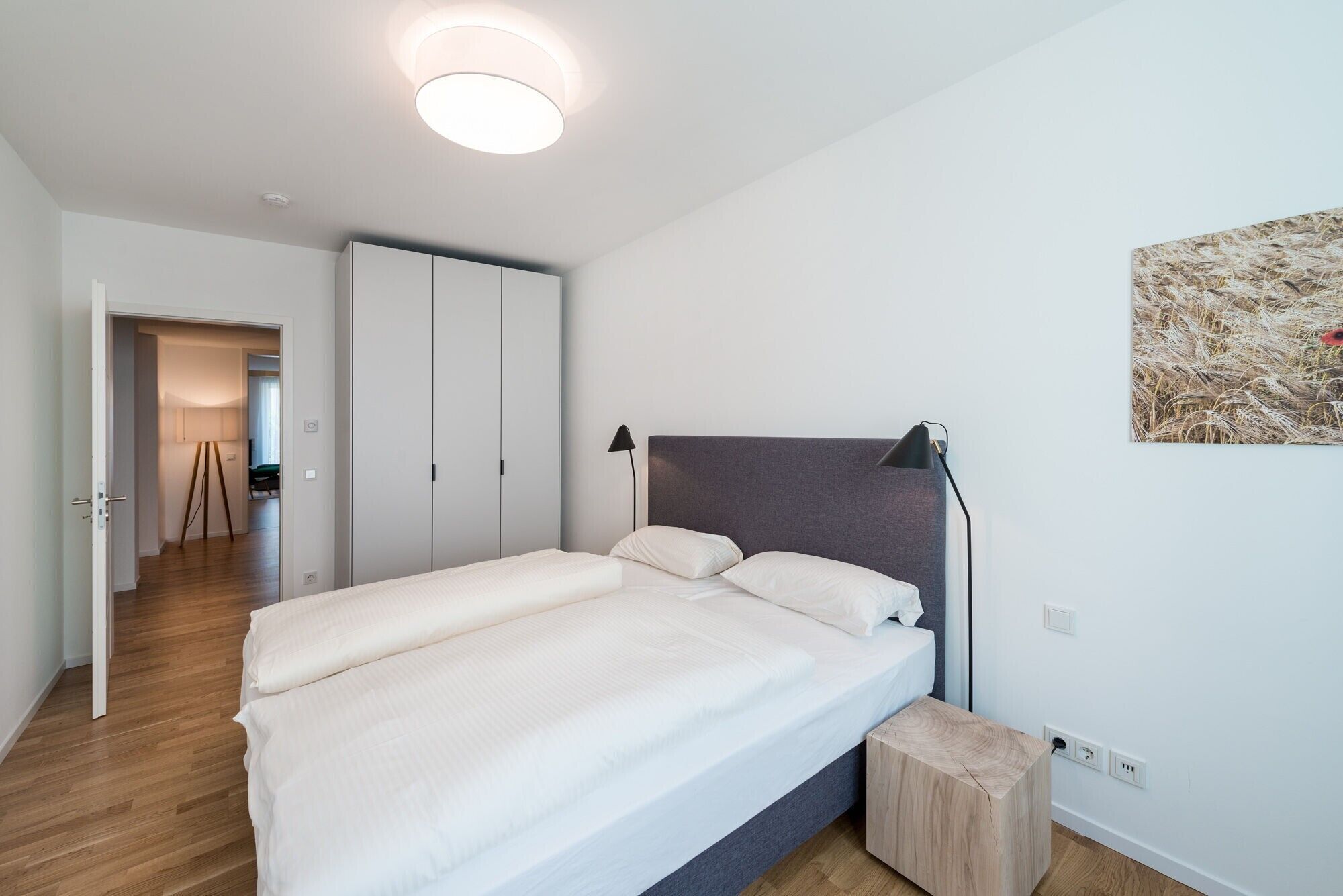 A bedroom with a bed, bedside lamps, a bedside table, a wardrobe, and a painting on the wall.