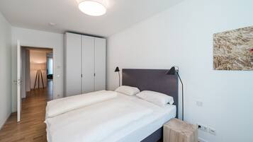 A bedroom with a bed, bedside lamps, a bedside table, a wardrobe, and a painting on the wall.