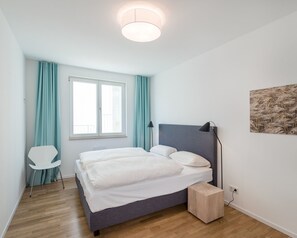 Una camera da letto con un letto, una sedia, un comodino, una finestra e un quadro appeso al muro.