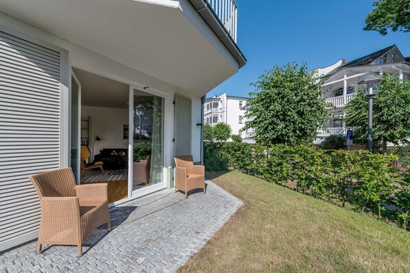 Une maison moderne dotée d’un patio, de deux fauteuils en osier et d’une porte en verre donnant sur un espace intérieur.