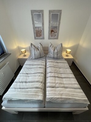 Una cama doble con ropa de cama a rayas, dos lámparas de noche y dos cuadros en la pared.