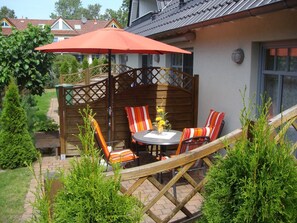 Un patio con una mesa, sillas, una valla de madera y un paraguas rojo.