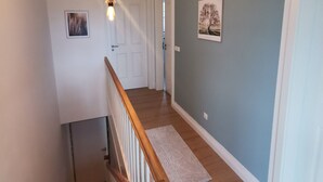 Un couloir avec un escalier en bois, une porte blanche, un luminaire et un tableau encadré au mur.