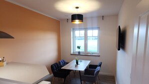 Une cuisine moderne avec un plan de travail blanc, une table à manger avec des chaises, un luminaire suspendu et une fenêtre donnant sur un paysage agréable.