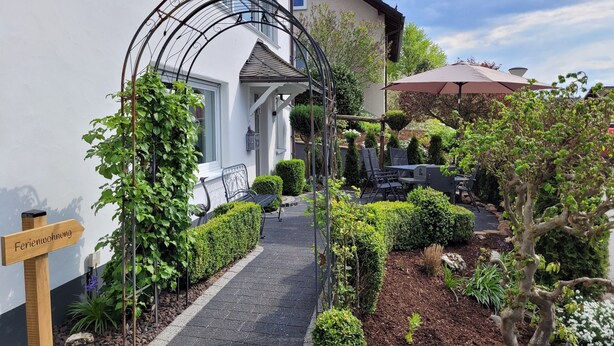 A garden entrance with a pathway, a wooden sign, and a metal pergola. - Friedhoff Apartment, 80 sqm with Mountain View, Private Terrace and Wi-Fi (Schmallenberg)