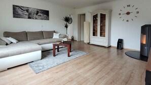 A living room with a sofa, coffee table, fireplace, and a clock on the wall. - Friedhoff Apartment, 80 sqm with Mountain View, Private Terrace and Wi-Fi (Schmallenberg)