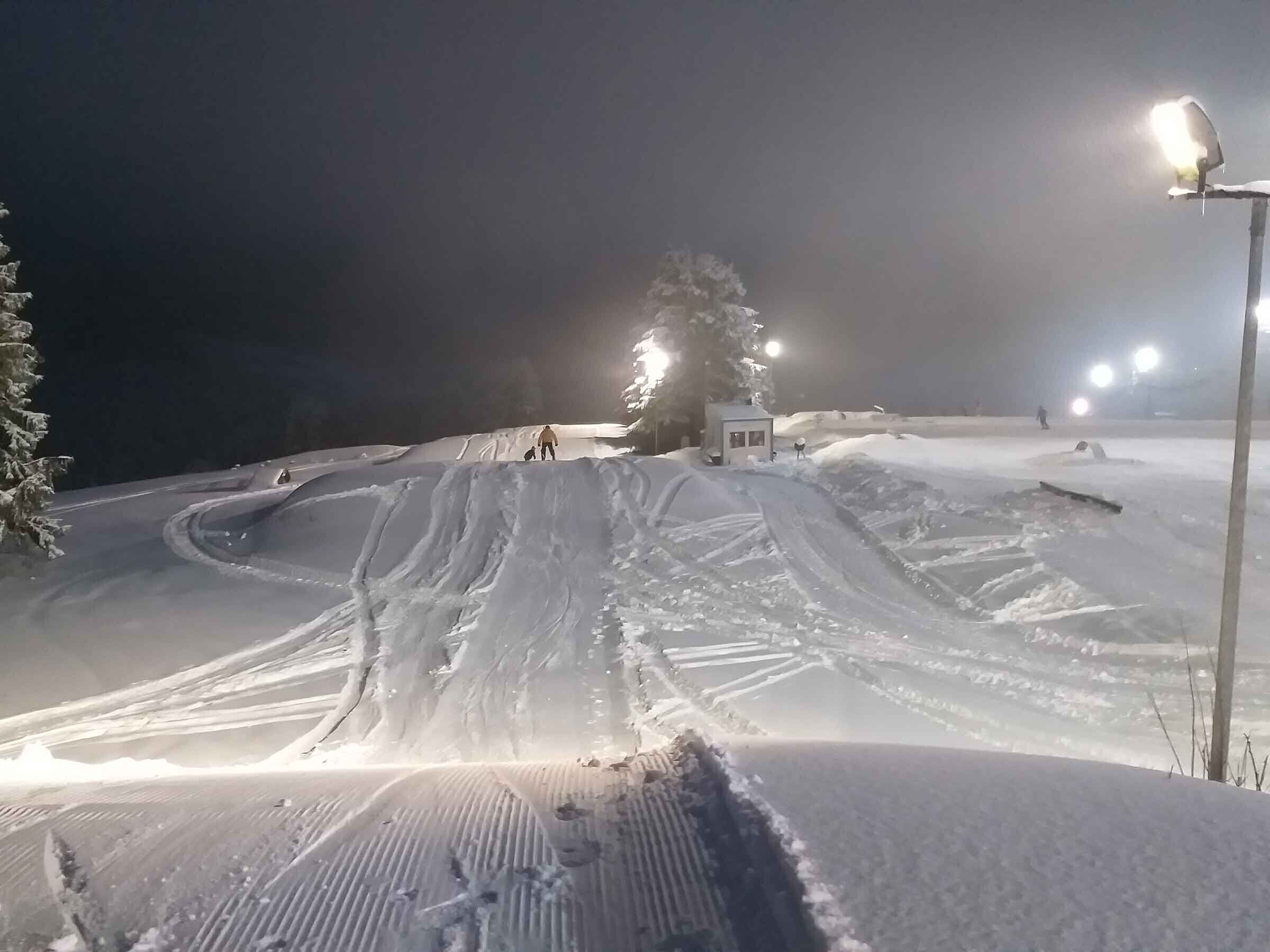 Une piste de ski enneigée, illuminée par des projecteurs, la nuit.