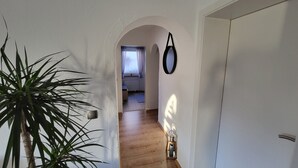 A hallway with a plant, a mirror, and a door leading to a room with a window and a radiator. - Friedhoff Apartment, 80 sqm with Mountain View, Private Terrace and Wi-Fi (Schmallenberg)