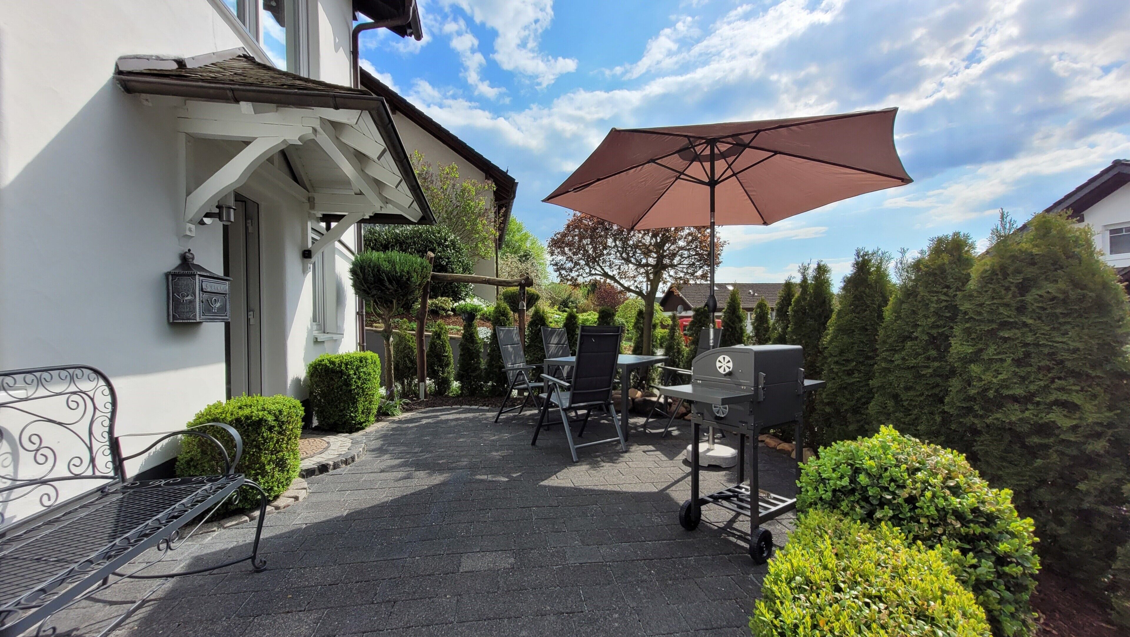 Une terrasse avec un barbecue, des sièges d’extérieur et un grand parasol.