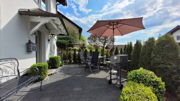 Eine Terrasse mit Grill, Sitzgelegenheiten im Freien und einem großen Sonnenschirm.