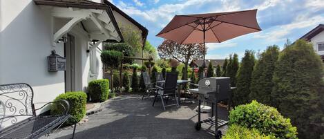 Une terrasse avec un barbecue, des sièges d’extérieur et un grand parasol.