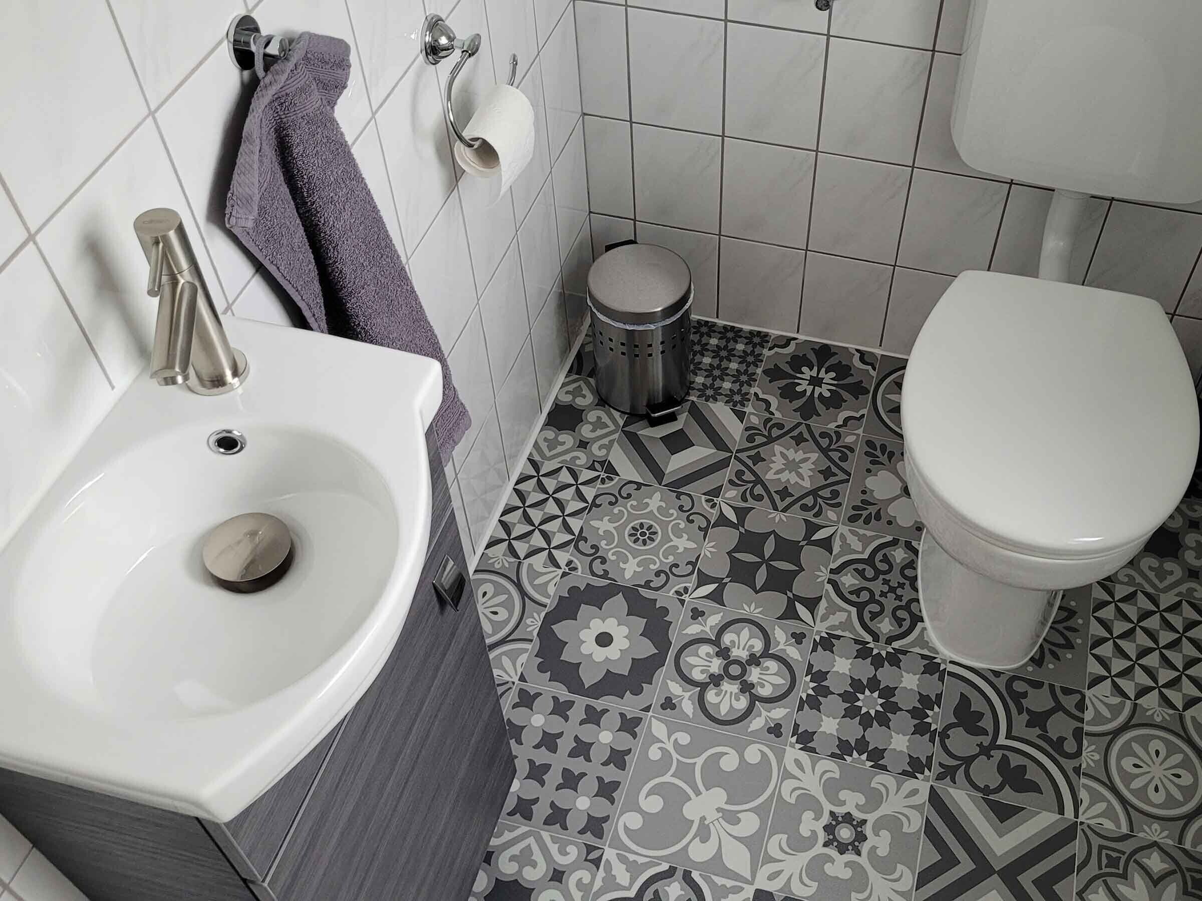 Un baño con lavamanos blanco, inodoro y baldosas de suelo estampadas.