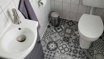 Un baño con lavamanos blanco, inodoro y baldosas de suelo estampadas.