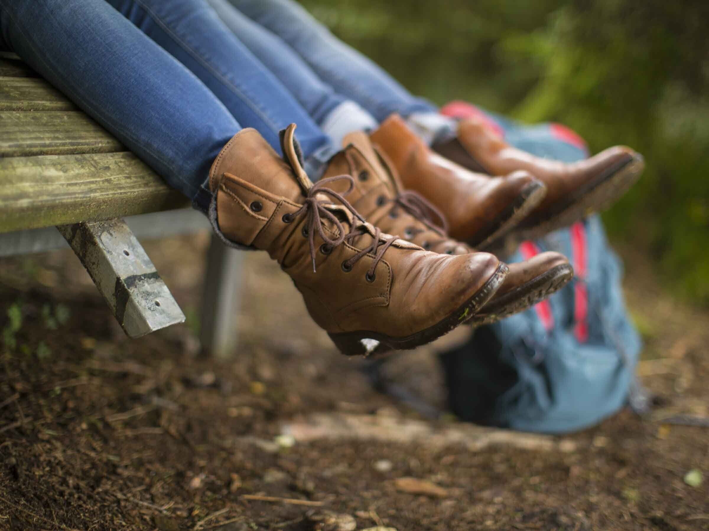 Una persona sentada en un banco, con botas marrones y vaqueros azules.