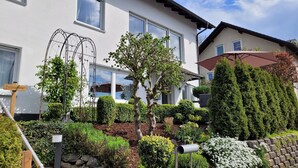 A modern two-story house with a well-maintained garden, including various shrubs and a small tree. - Friedhoff Apartment, 80 sqm with Mountain View, Private Terrace and Wi-Fi (Schmallenberg)