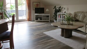 A living room with a sofa, coffee table, TV, bookshelf, and a dining area with chairs.