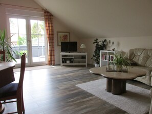 Una sala de estar con sofá, mesa de centro, televisor, estantería y un comedor con sillas.