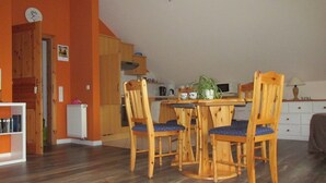 A dining area with a wooden table and chairs, a kitchen in the background, and a radiator on the floor.