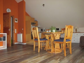 Un coin repas avec une table et des chaises en bois, une cuisine à l’arrière-plan et un radiateur au sol.