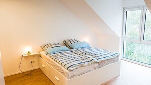 A bedroom with a bed, wooden flooring, a nightstand, and a window. - Apartment 'Ferienwohnung Weitblick Koblenz' with Balcony and Wi-Fi (Koblenz)