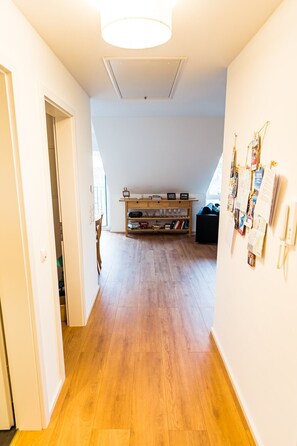 Un couloir doté d’un plancher en bois, d’un luminaire au plafond, d’une bibliothèque et d’un tableau d’affichage.