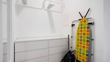 Una habitación con un armario blanco, un aspirador y una tabla de planchar colorida.