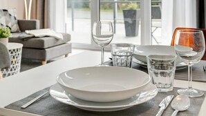 Una mesa de comedor dispuesta con platos, vasos y cubiertos, con vistas al exterior a través de amplios ventanales.