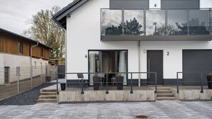 Un edificio moderno con un balcón, una puerta marcada con el número 2, y una zona pavimentada con escaleras que conducen a la entrada.
