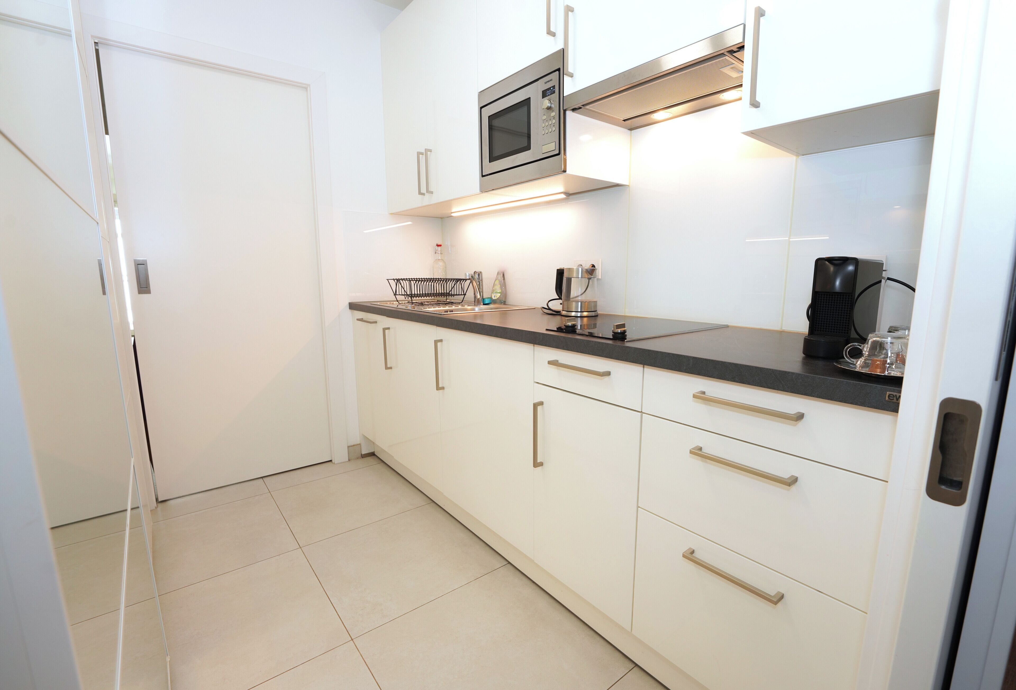 A kitchen with white cabinets, a microwave, a coffee maker, and a sink.